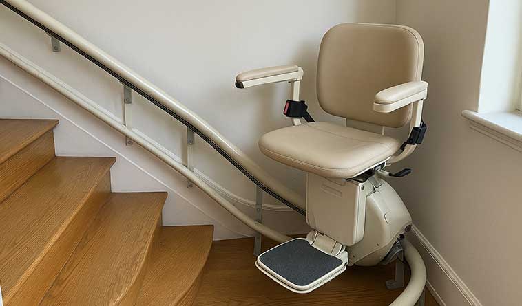 Gebrauchter Treppenlift mit beigem Sitz und heller Armlehne an einer geraden Treppe.